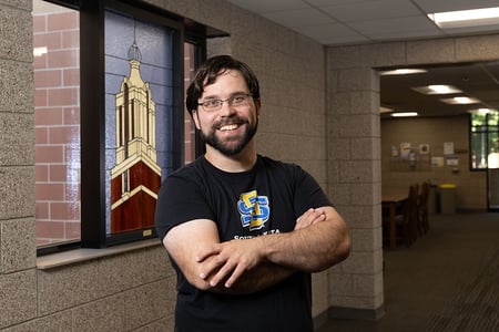 Employee Eric Fish posing in front of stained glass window in residence hall lobby