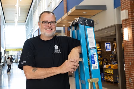 Employee Mike Kellen posing with ladder on main street of student union